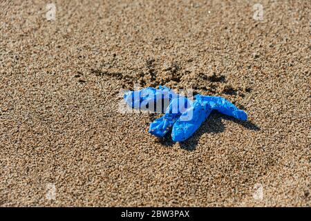 closeup of a blue used latex glove thrown on the wet sand of the seashore of a beach Stock Photo
