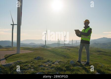 Technician Engineer in Wind Turbine Power Generator Station standing with a tablet in his hands Stock Photo