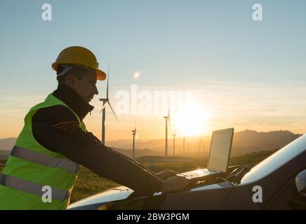 Technician Engineer in Wind Turbine Power Generator Station checks the status of the turbines using a laptop Stock Photo