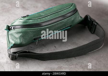Belt bag made of dark green textured leather, banana on a gray background. Stock Photo