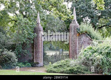 Old wrought iron gates mounted between two tall slim brick gate posts in an English country garden. Stock Photo