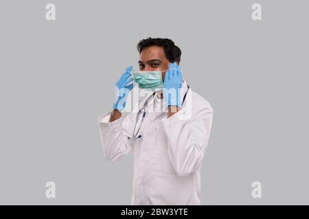 Doctor Puts on Medical Mask Wearing Gloves Isolated. Indian Man Doctor Medical Uniform Stock Photo