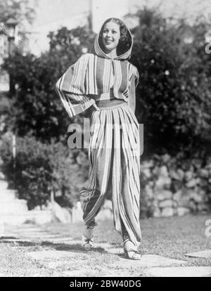 And now the Arab - Loretta Young lunches novel beach fashion. The flowing  robes and burnous of the Arab inspired this novel striped beach ensemble  which Loretta Young, the film actress, gaily