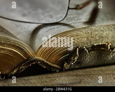 Edge of old worn tattered book with reading glasses Stock Photo