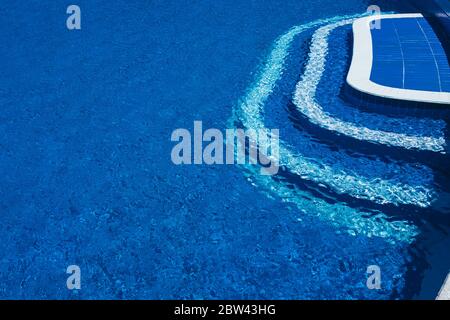 Steps to the pool, blue clear water in the outdoor swimming pool, safe descent to the pool, close-up steps through the water. White steps on a blue ba Stock Photo