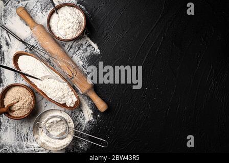 Different types of flour in wooden bowls on black table, top view Stock Photo