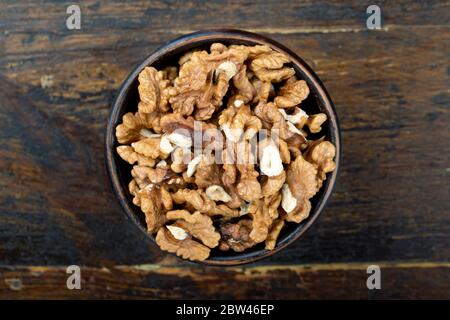 kernels of peeled walnuts in a clay plate on a brown wooden background. view from above Stock Photo