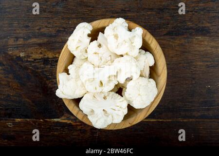inflorescences of raw cauliflower in a wooden plate on a brown wooden table. view from above Stock Photo
