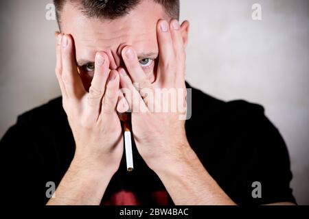 secret smoker with a cigarette in his mouth shamely covers his face with his hands and looks through his fingers Stock Photo