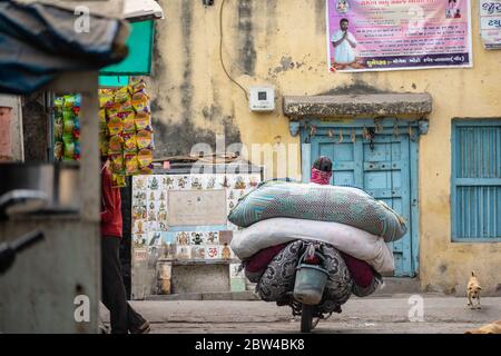 Somnath, Gujarat, India - December 2018:  A man on a motorcycle carrying big sacks of laundry past the old vintage doors of the old town. Stock Photo