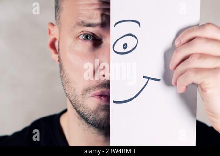 a smile painted on paper partially covers the face of a sad man, close up Stock Photo