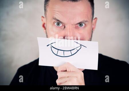 angry man covers his mouth with a sheet with a painted smile. close up Stock Photo