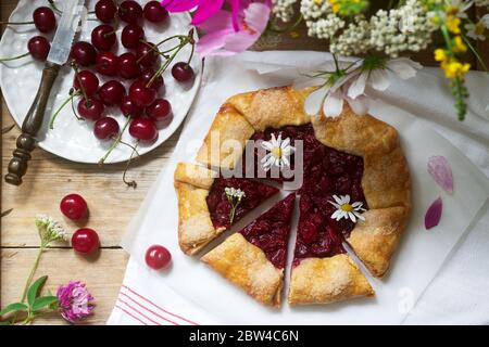 Sweet pie galette with juicy berry filling, berries and wild flowers on a wooden background. Rustic style. Stock Photo