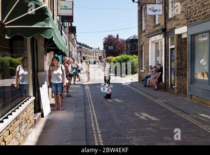 Skipton, North Yorkshire, UK. Social-distancing shoppers queue in Spring sunshine outside a butchers shop on Friday market day amid the Covid-19 lockdown. Credit: John Bentley/Alamy Live News Stock Photo