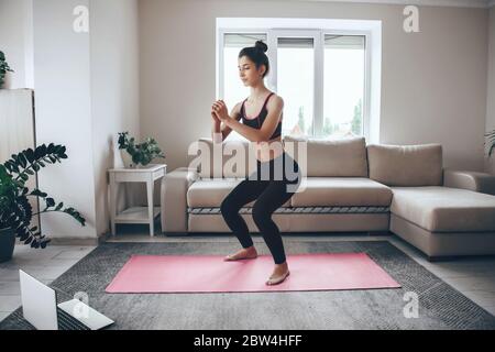 Brunette girl doing warming exercises at home on a pink sport carpet with a laptop Stock Photo