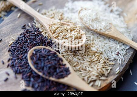 Black wild rice, brown wild rice and white jasmine rice in wooden spoon flat lay. Creative layout. Food concept. Focus on brown rice. Stock Photo
