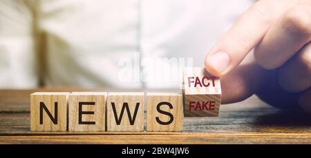 A man puts wooden blocks with the words News - Fact or fake. False / true information concept. Yellow press. Stock Photo