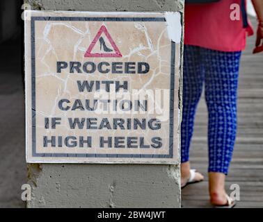 Sign to warn of the danger of wearing high heels. A lady with flat heels walks on the boardwalk Stock Photo