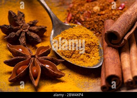 in a rustic wooden bowl, in the foreground, some star anise stars, cinnamon sticks and some powder spices Stock Photo