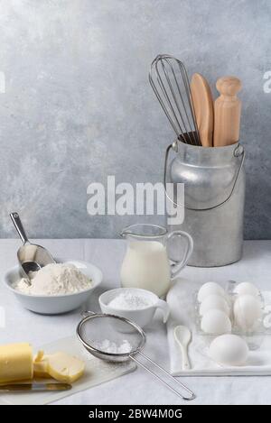 in the kitchen on the gray textured background, some utensils, flour, milk and eggs and various ingredients ready for the preparation of homemade culi Stock Photo