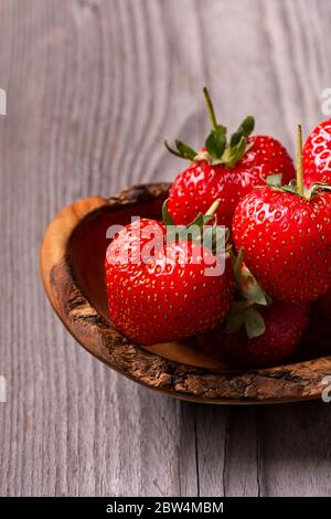 in the foreground, a wooden bowl with ripe strawberries on the rustic wooden background Stock Photo
