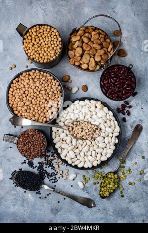 top view, in different bowls, on a textured gray background, variety of raw and colorful dry legumes rich in protein Stock Photo