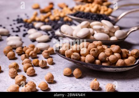 assortment of dried legumes in spoons arranged in a row with focus on the foreground on a gray textured background Stock Photo