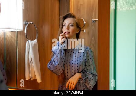 Portrait of Young Beautiful Woman in Dress Doing Make-up Standing Near Mirror Stock Photo