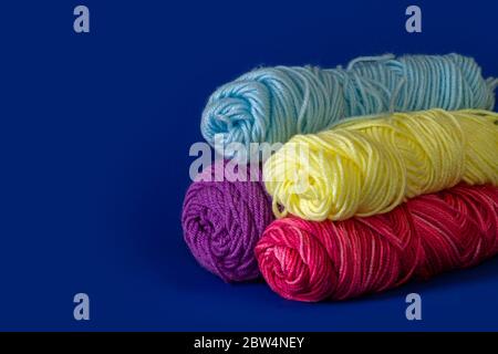 Stack of blue, yellow, purple, and red yarn with a dark blue background Stock Photo