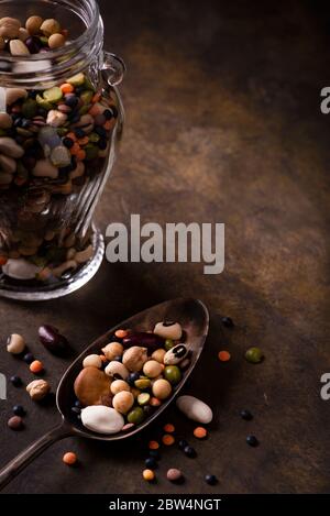 on a textured brown background, in the foreground, with grazing light, varieties of dry and raw legumes rich in proteins. copy space Stock Photo