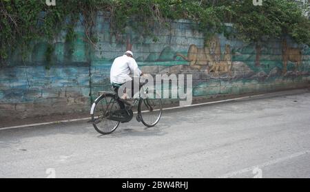 Old man going to home by cycle. man wearing face mask and riding cycle in empty road. corona lock down. Stock Photo
