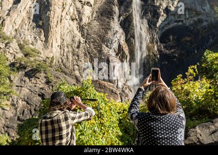 Tourists take pictures with their smartphones from the base of the Bridalveil Fall in Yosemite National Park Stock Photo