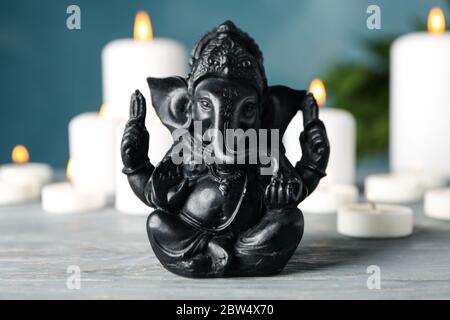 Hindu god Ganesha on white wooden table. Candles on background Stock Photo