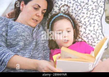 Mother and daughter lying on bed reading a story book. Top-down shoot. Home schooling concept with empty copy space for Editor's text. Stock Photo