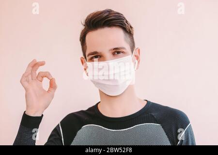 Portrait of happy young sports man in medical face mask showing okay sign and smiling. Confident fitness instructor in protective mask gesturing ok sy Stock Photo