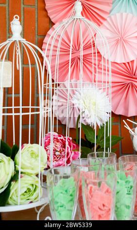 White metal cage with a white flower and another pink flower among the colorful decoration of a party.