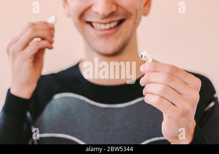 Closeup happy sports man wearing wireless earbuds and smiling at home. Young fitness man holding bluetooth earphones in hands. Listening music for mot Stock Photo