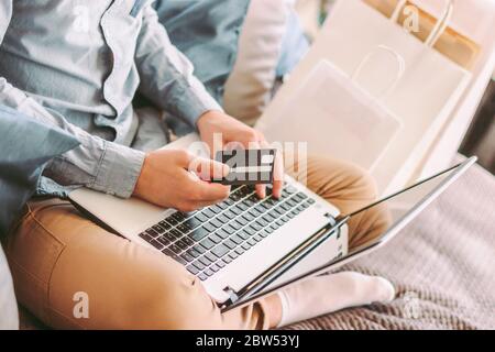 Closeup man shopper hold credit card in hand, typing on laptop keyboard, shopping online from home. Stylish hipster man sit on couch, using computer f Stock Photo