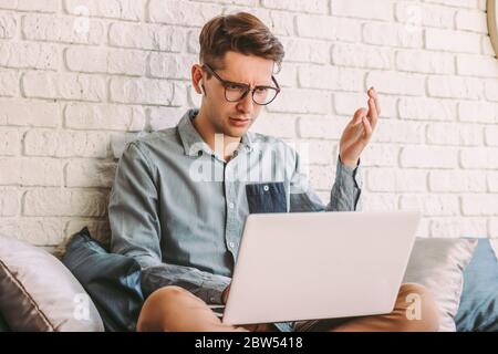 Angry confused businessman freelancer feel irritated while use laptop for work at home. Puzzled impatient hipster man in glasses impressed by bad news Stock Photo