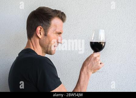 profile of a handsome Caucasian man wearing a black shirt looking at a glass of red wine with copy space Stock Photo