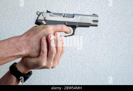 2 Caucasian male hands holding and aiming a semi-automatic pistol against a solid background with copy space Stock Photo