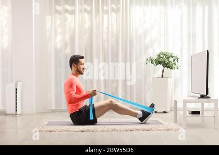 Man exercising with an elastic band in front of a tv at home Stock Photo