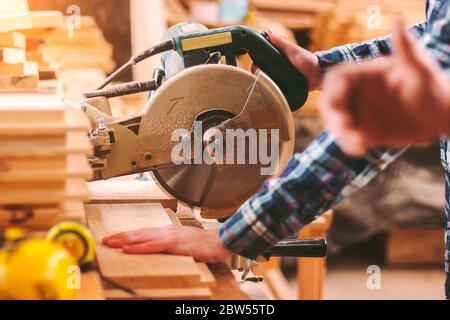 Closeup of professional cabinet makers working with electric circular saw at woodworking workshop. Skilled carpenter cutting wooden board with circula