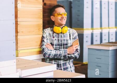 Happy young man sawmill factory business owner dreaming about big future with crossed arms and smiling. Young man warehouse manager inspecting wood st Stock Photo