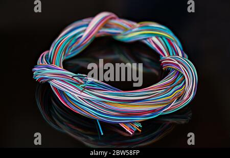 Electric cable harness of tangled colorful wires. Round braided multicore wiring loom of insulated copper conductors. Reflection on black background Stock Photo