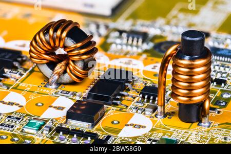 Toroidal and cylindrical inductor on circuit board of computer mainboard detail. Soldered induction coils with copper wire winding, chips, transistors. Stock Photo