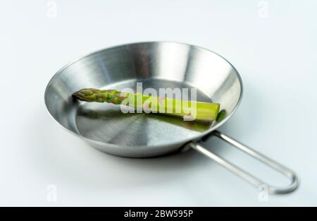 concept photo, huge asparagus lying on a small steel pan on a white background. Stock Photo