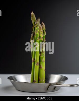 concept photo, a bunch of huge asparagus stands in the center of a small steel pan on a black and white background. Stock Photo