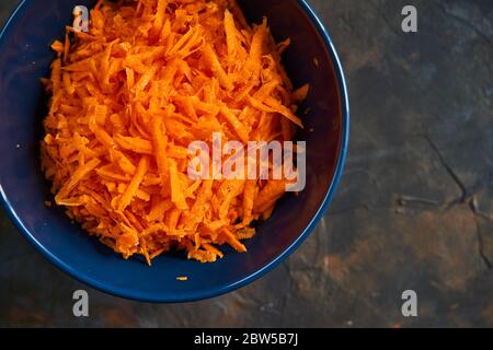 Grated carrots in a blue plate on a dark background. Stock Photo