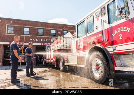One firefighter cleaning a fire truck with water from a hose as another looks on waiting to help. Stock Photo